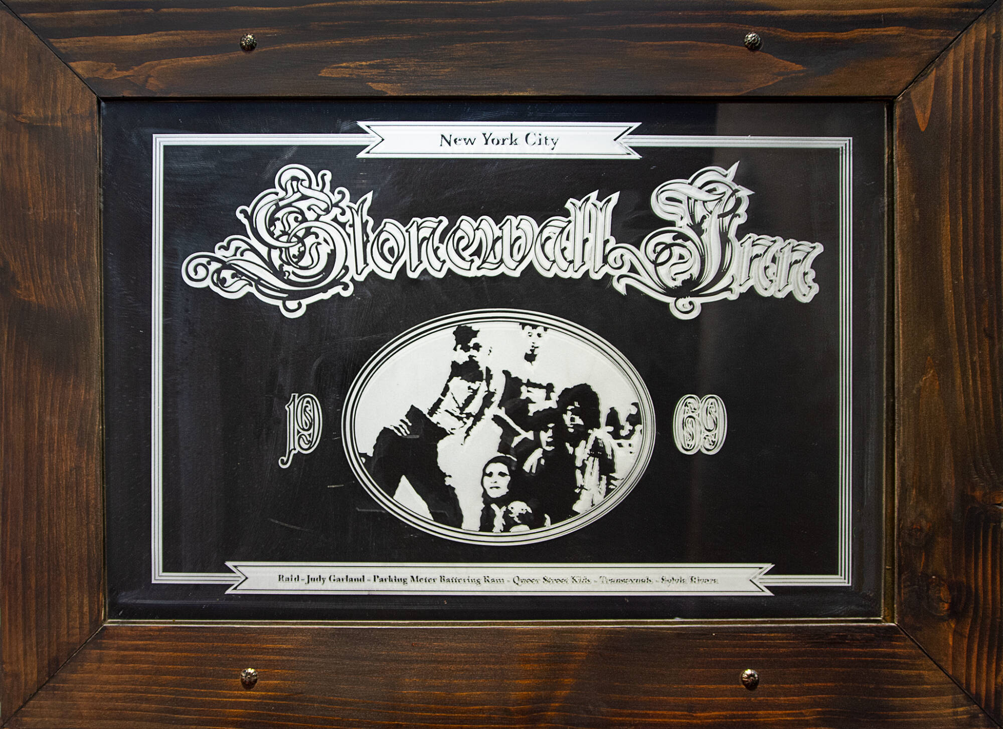 Bar-style mirror with sand blasted image depicting a group of people posing in an oval frame and text that reads, "New York City, Stonewall Inn, 1969, Raid